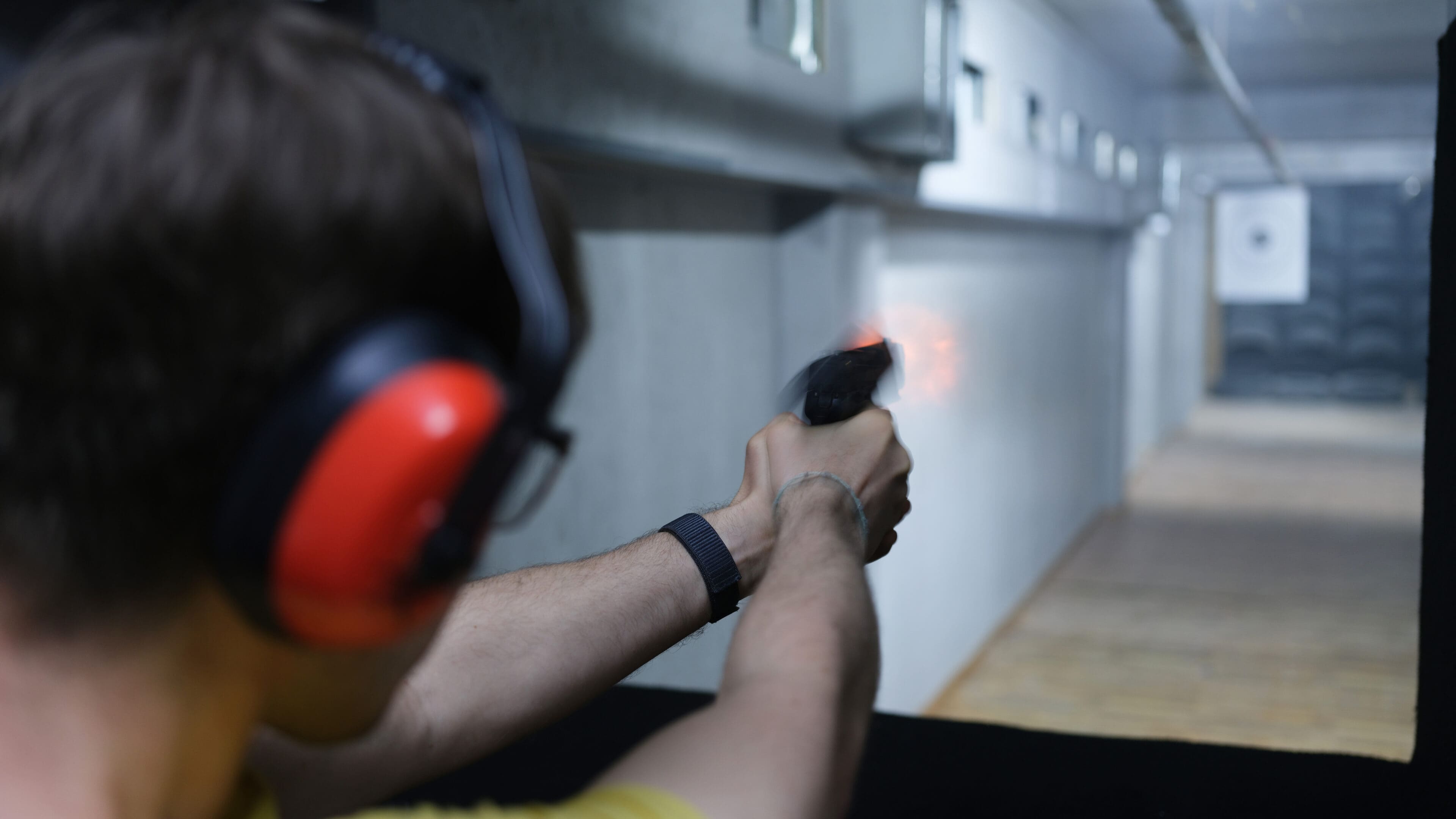 Shooter man holding gun in hand and shooting at a target rear view. Pistol shooting practice