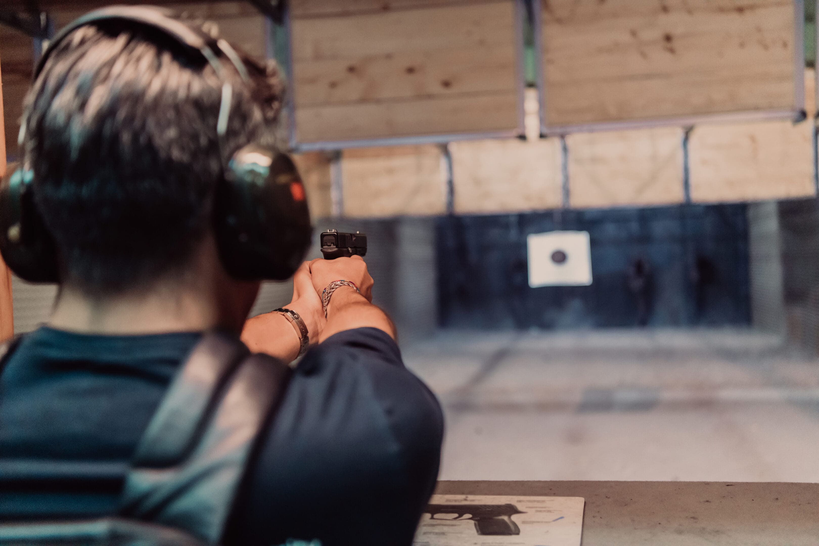 A man practices shooting a pistol in a shooting range while wearing protective headphones.