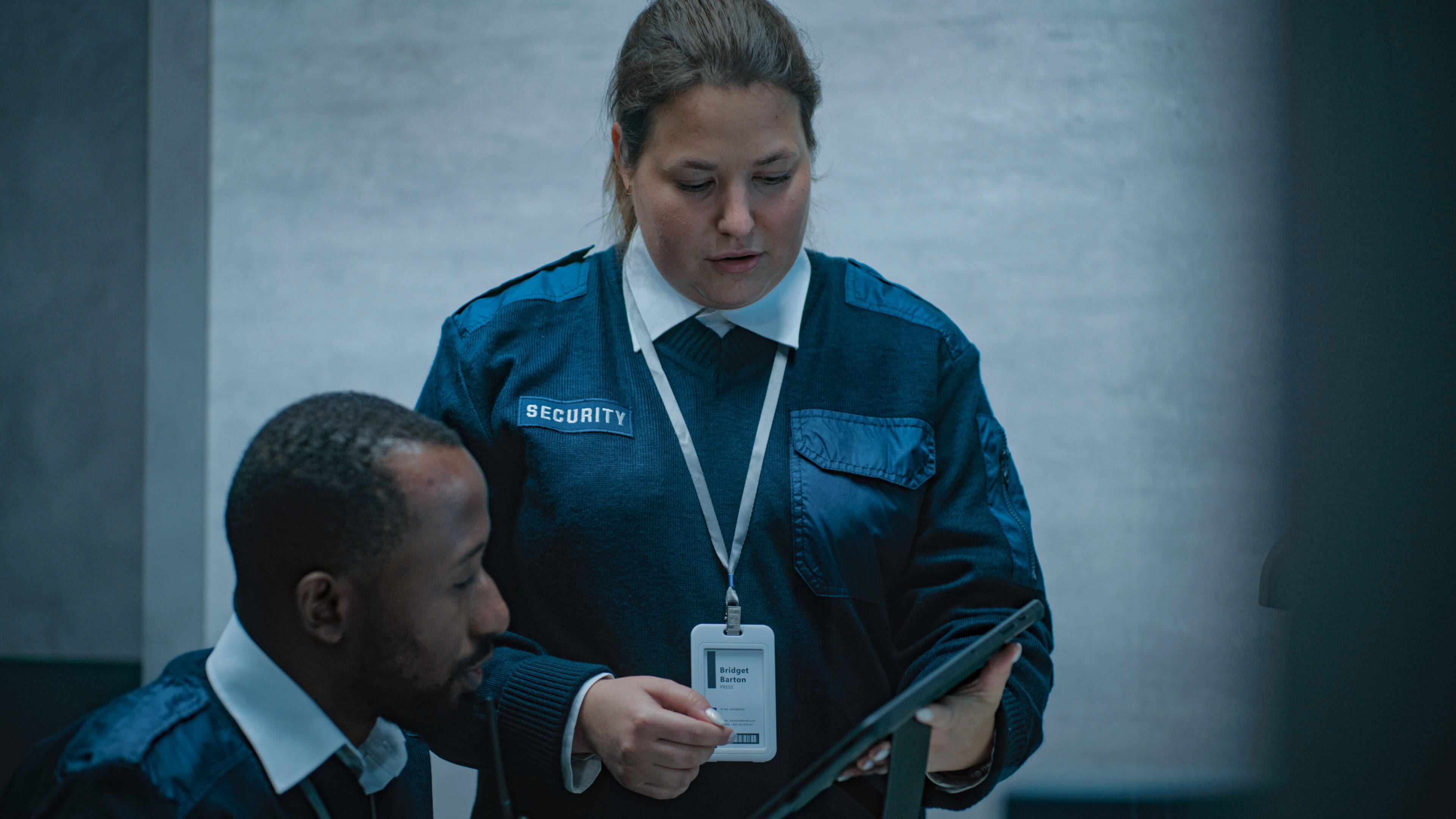 Female security worker talks with African American male colleague, uses tablet computer. Multiethnic surveillance operators control security cameras working in modern monitoring center. CCTV system.