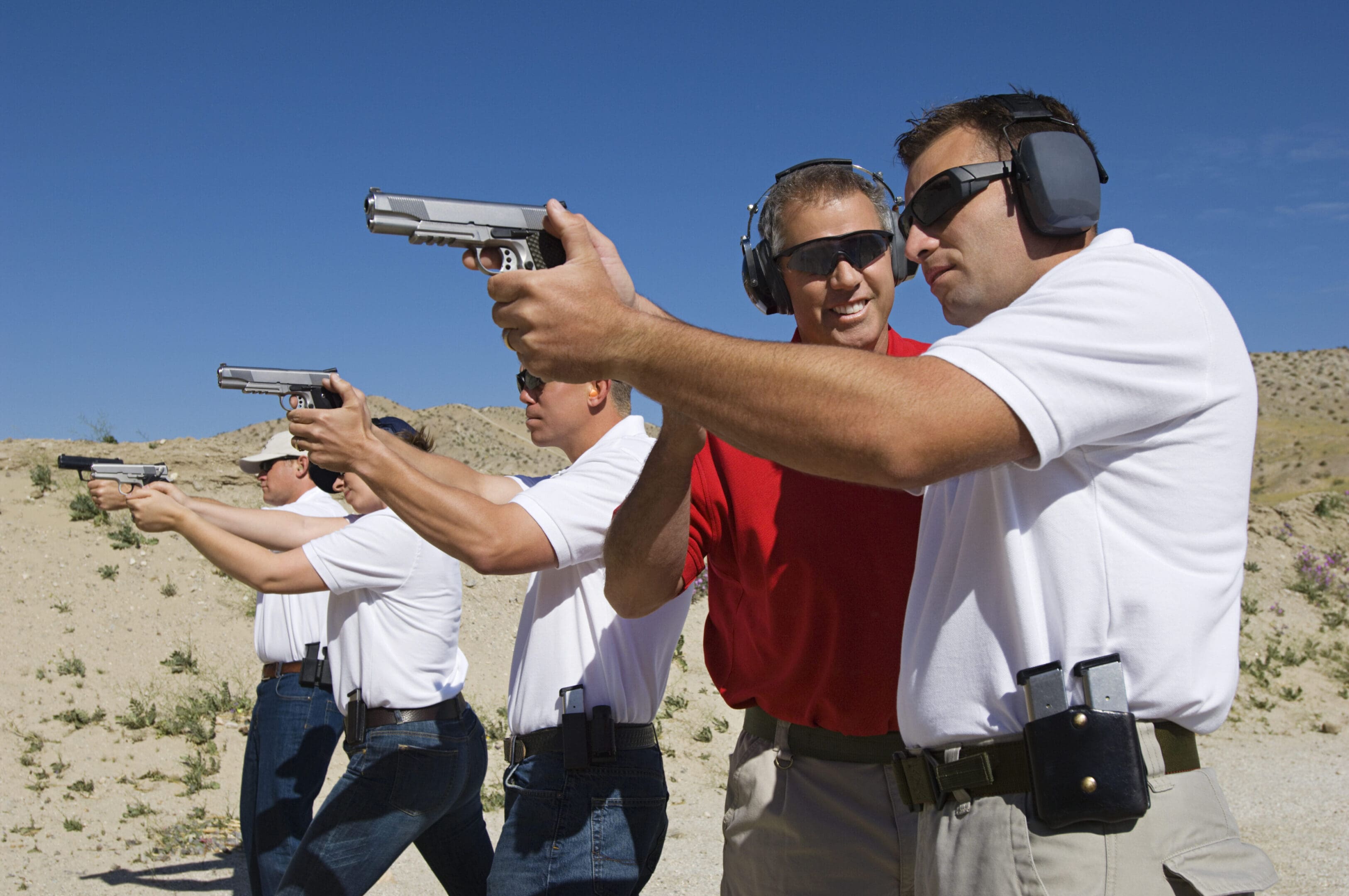 Instructor assisting men aiming hand guns at firing range